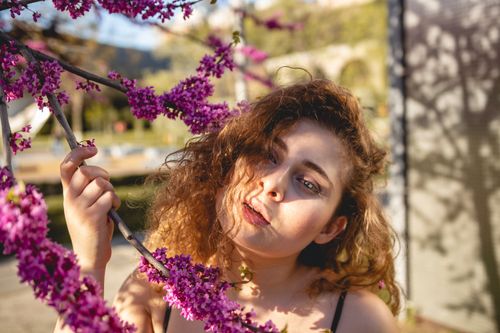Free Caucasian woman with curly hair admiring vibrant cherry blossoms outdoors in sunny Georgian spring. Stock Photo