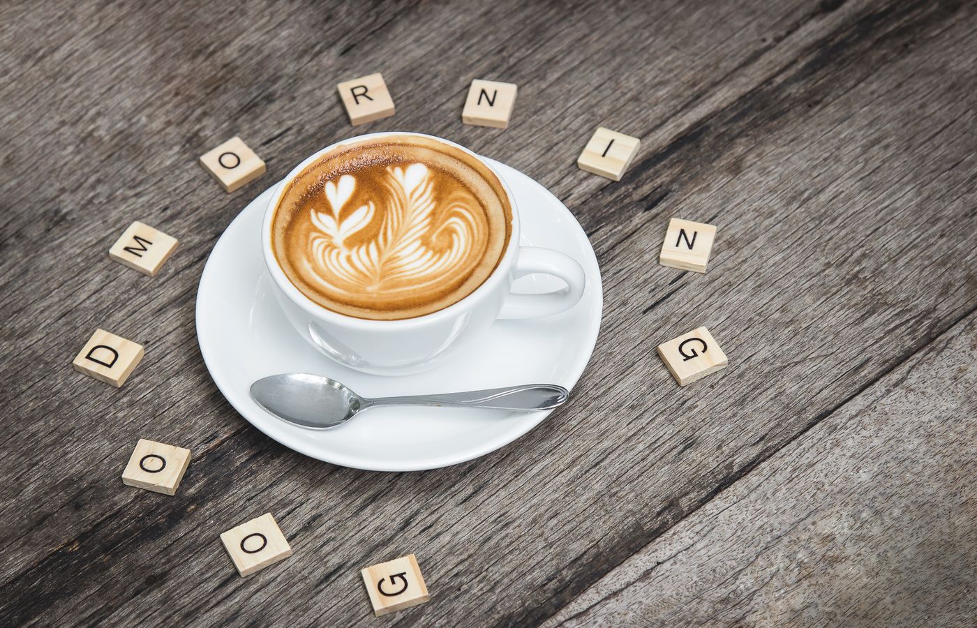 Cup of cappuccino with latte art surrounded by Scrabble letters spelling 'Good Morning'.