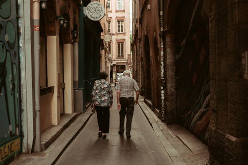 Free A serene scene of an elderly couple walking down a historic alley in Lyon, France. Stock Photo