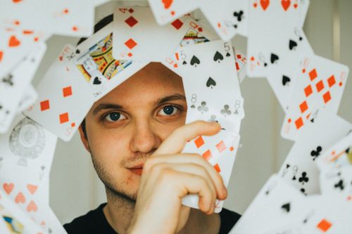Free A young man peering through a cascade of playing cards in a creative shot. Stock Photo