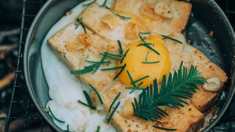 From above appetizing grilled toasts under egg with rosemary cooked on frying pan on barbecue grid