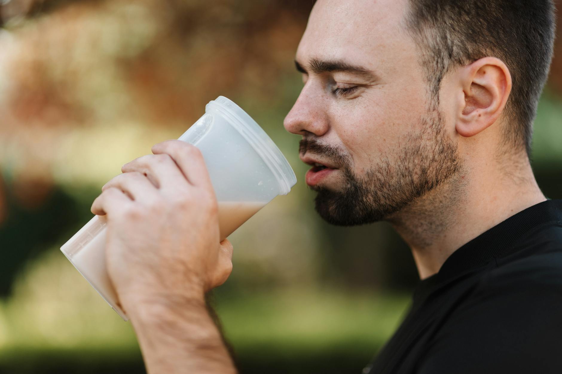 Bearded man drinking a protein shake outdoors on a sunny day, showcasing healthy living.