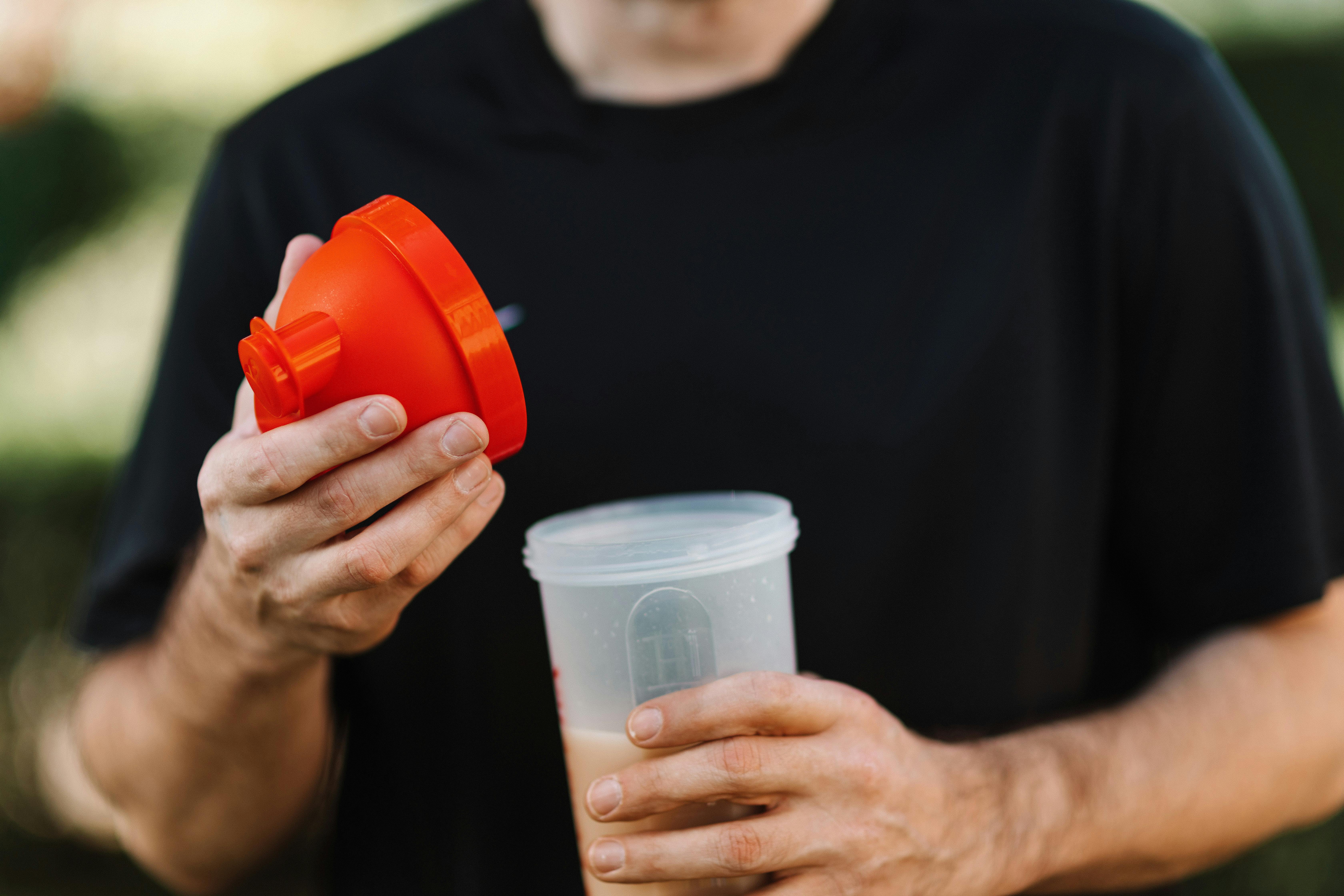 Hands holding red supplement measuring scoop over clear container, showing supplement preparation that could be risky for people with existing health conditions.