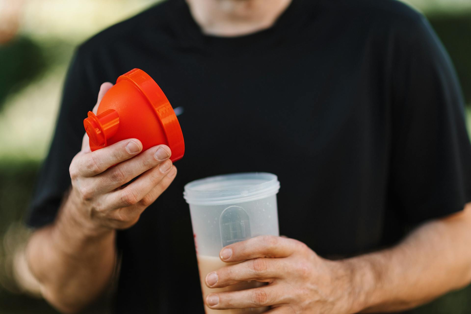 Man in Black Crew Neck Shirt Holding Red Lid and a Plastic Tumbler