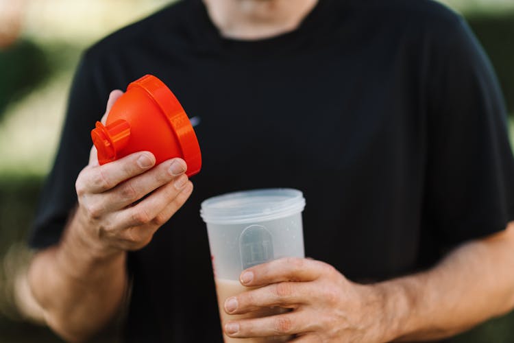 Man In Black Crew Neck Shirt Holding Red Lid And A Plastic Tumbler