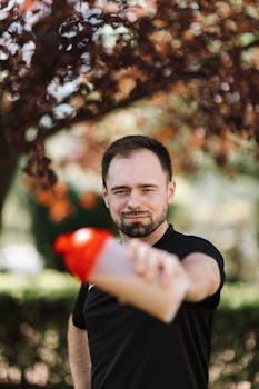 A man holding a protein shake tumbler outdoors in a sunny park setting.