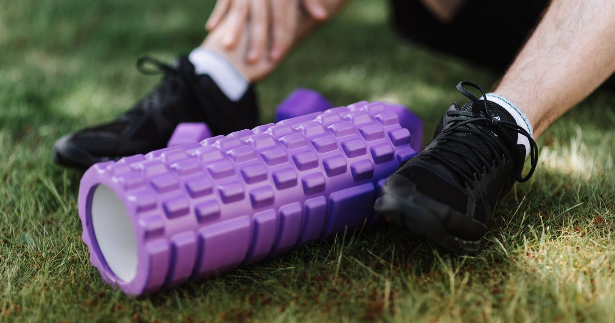 A purple textured foam roller on grass beside sneakers