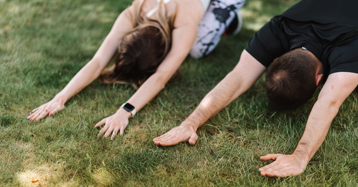Man and woman performing child's pose yoga on green grass. Outdoor wellness activity.