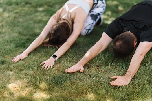 Man and woman performing child's pose yoga on green grass. Outdoor wellness activity.