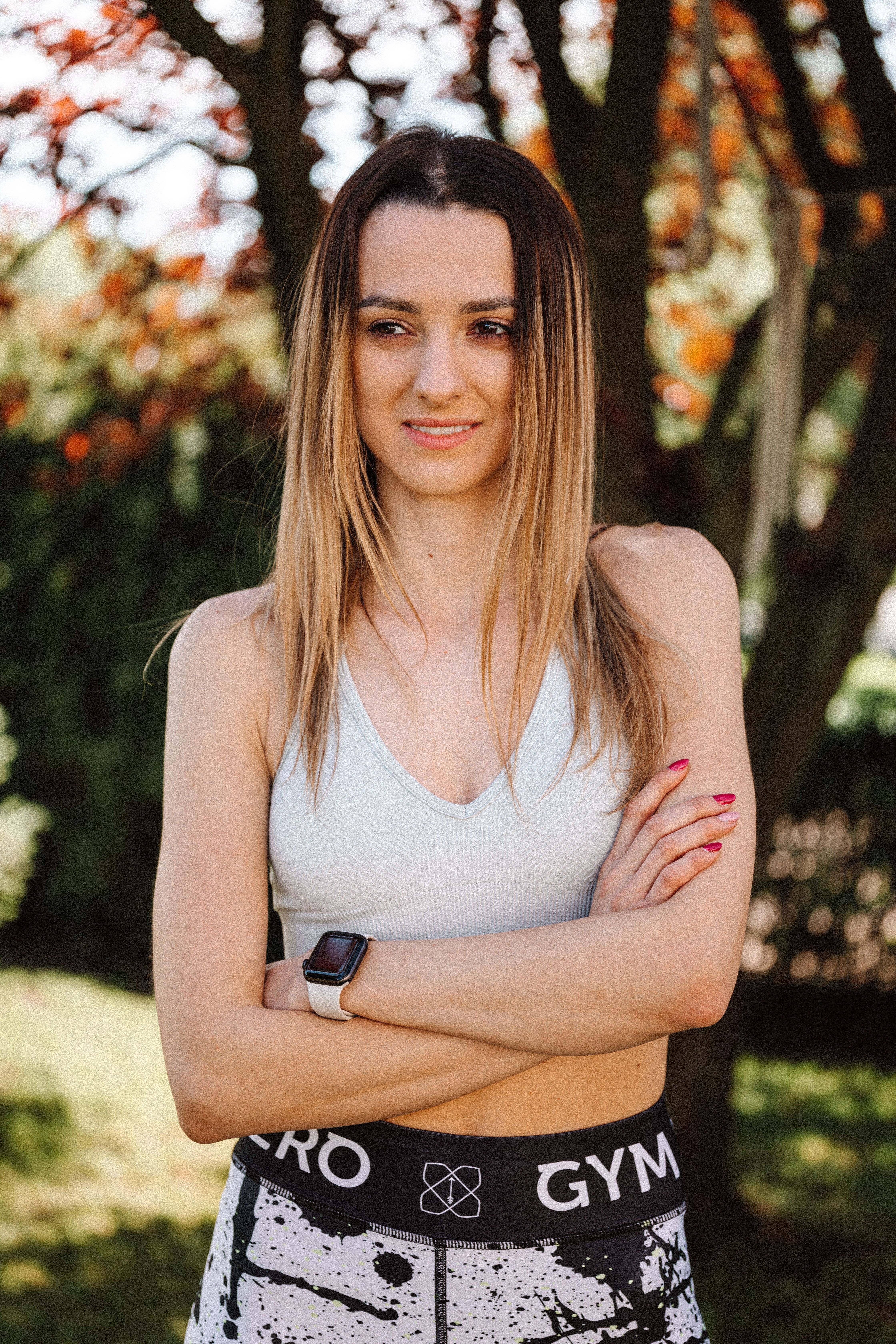 Young woman with arms crossed in activewear, enjoying a sunny outdoor day.
