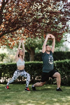 A couple in activewear stretching outdoors under a tree, embodying healthy living and wellness.