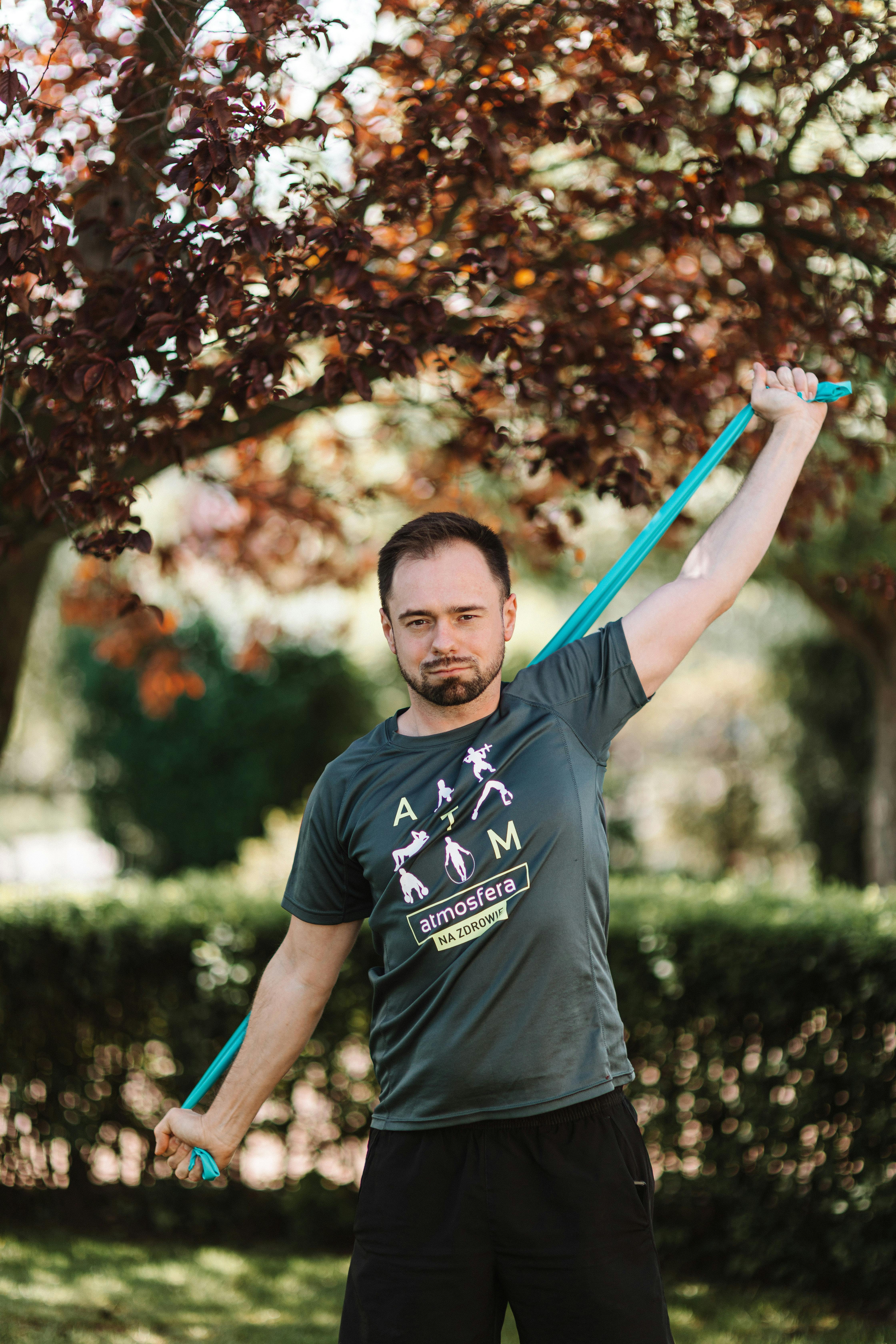 Adult male exercising with a resistance band outdoors in a park setting, promoting wellness and fitness.