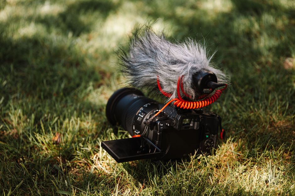 Close-up of a DSLR camera with a microphone attachment lying on grass, perfect for videography outdoors.