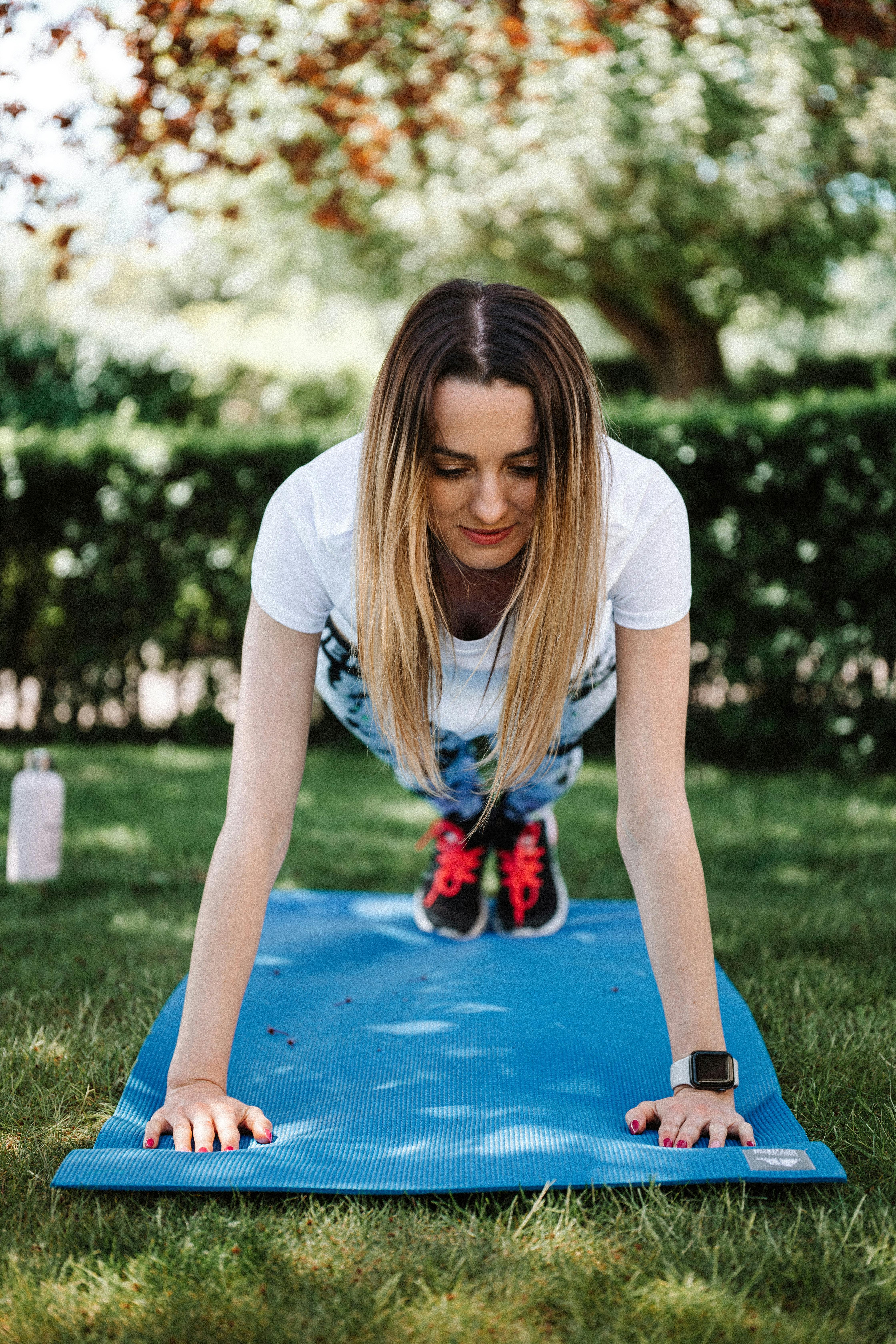 A woman performs a workout on a yoga mat outdoors in a sunny park.