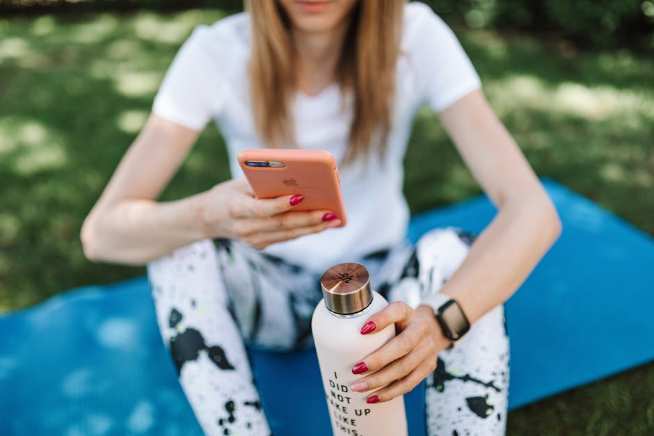 Shallow Focus Photo of a Woman Holding a Water Bottle while Using Her Iphone