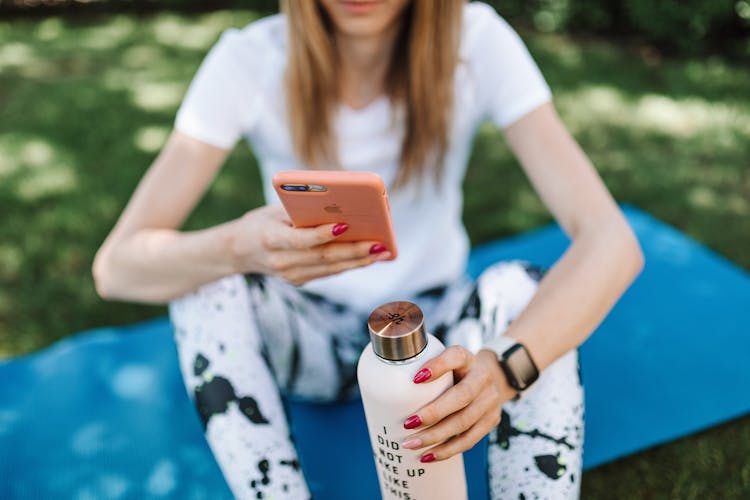 Shallow Focus Photo Of A Woman Holding A Water Bottle While Using Her Iphone