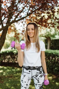 A woman exercising outdoors, lifting dumbbells, promoting healthy and active lifestyle.