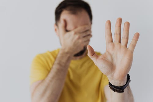 Man in Yellow Shirt Covering His Face with Hand and Showing Stop Sign Gesture