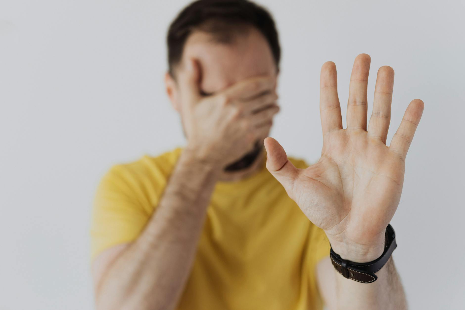 Close-up of a man covering his face and showing a stop gesture with his hand.
