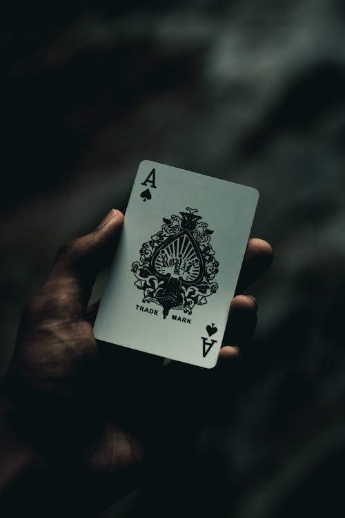 From above of crop anonymous person demonstrating ace of spades playing card against dark blurred background