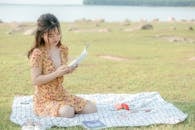 Tranquil young ethnic lady reading textbook on green lawn