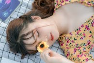 Peaceful young ethnic lady with flower in hand lying on blanket with closed eyes