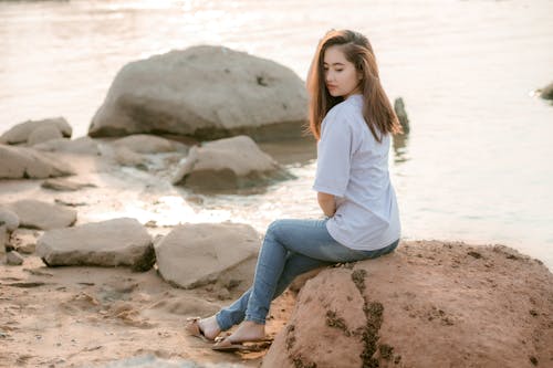 Free Pensive young Asian lady resting on rocky seashore Stock Photo