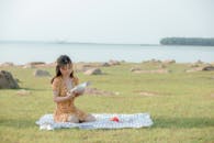 Concentrated young Asian female student reading book during picnic
