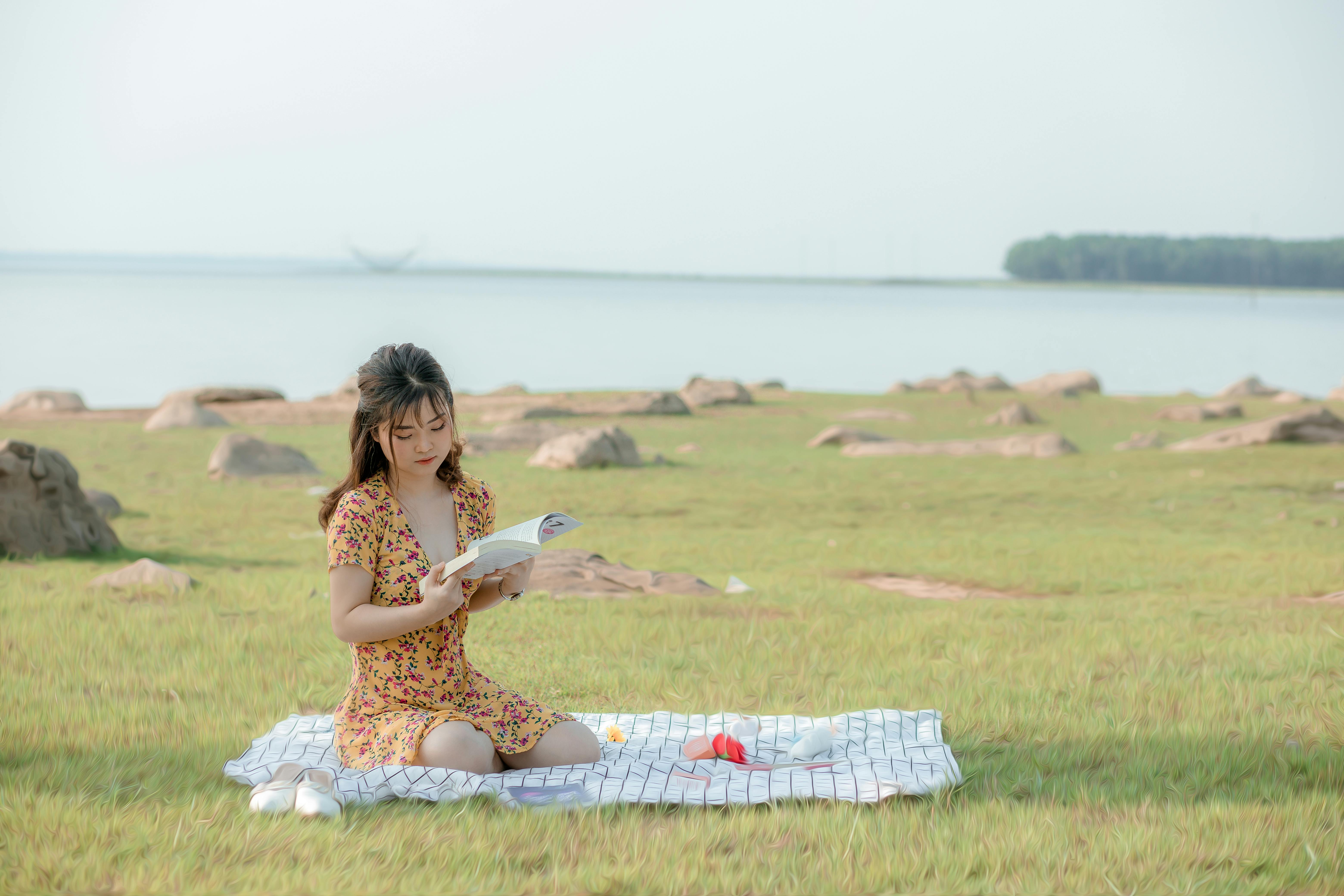 Concentrated young Asian female student reading book during picnic