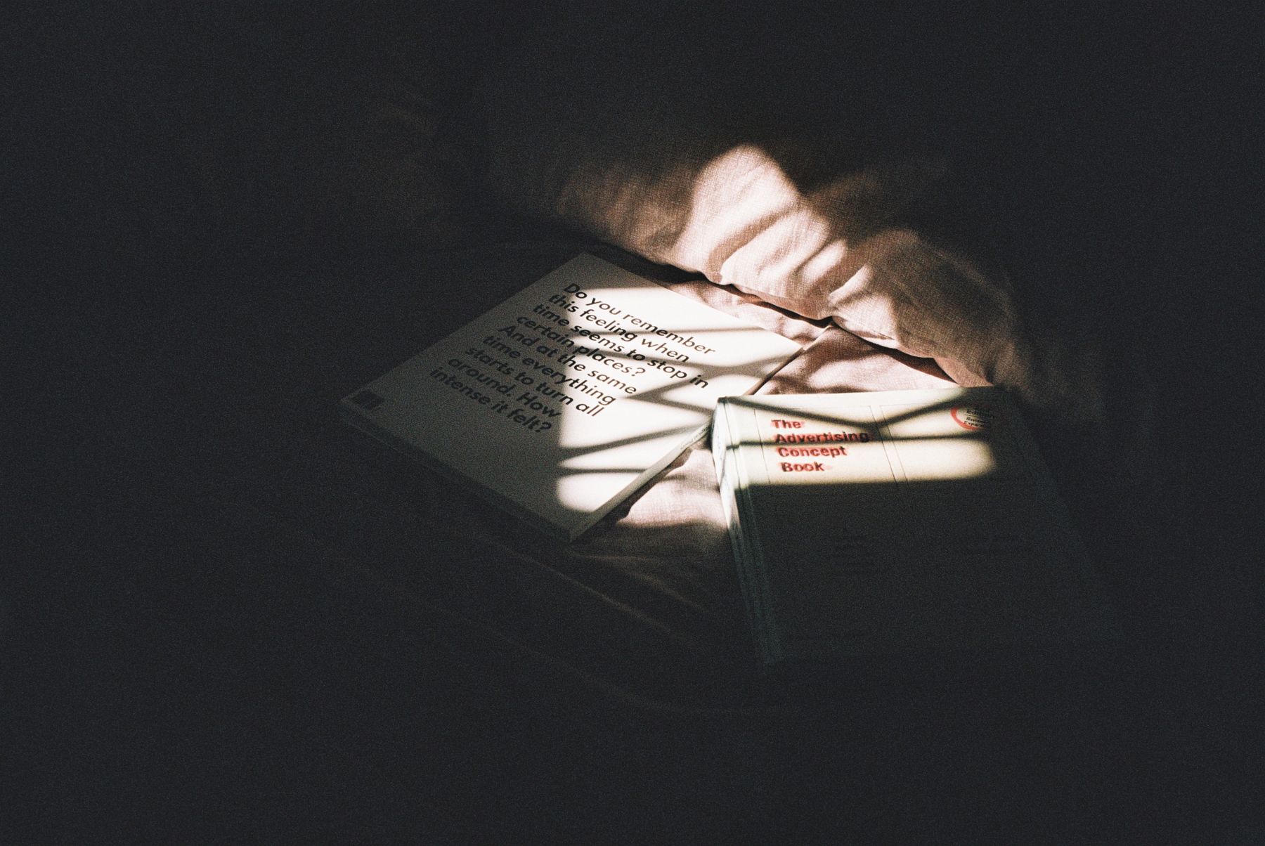 Books resting on rumpled bedding with a diagonal band of sunlight and shadow