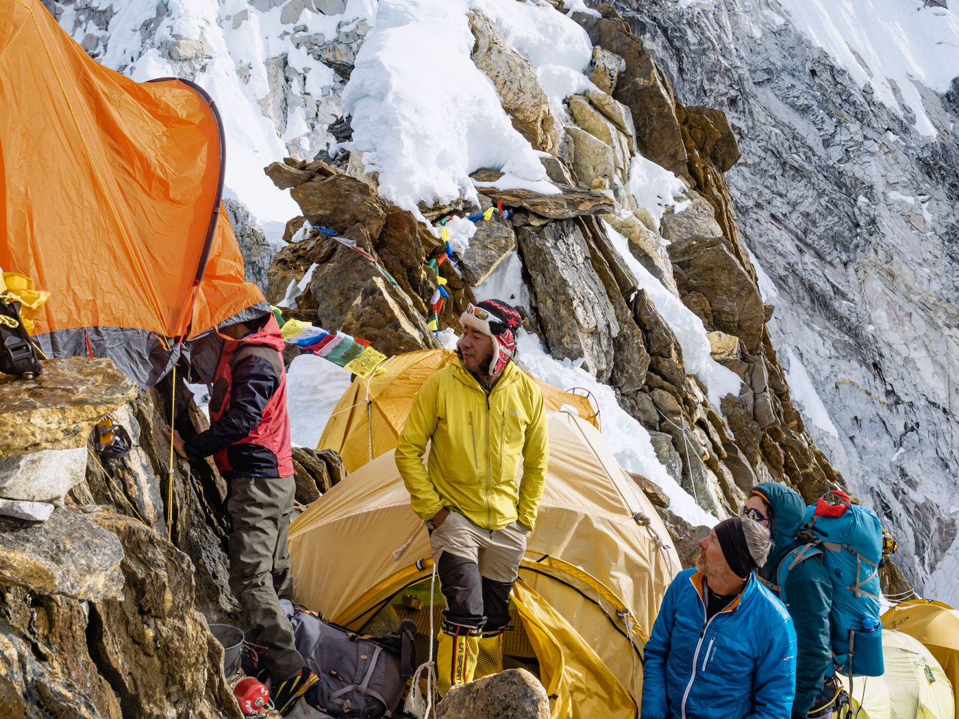 An expedition team setting up yellow tents on a snow-covered Himalayan slope