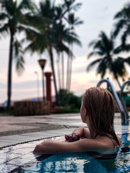 A woman enjoys leisure time in a swimming pool surrounded by palm trees in Malaysia.