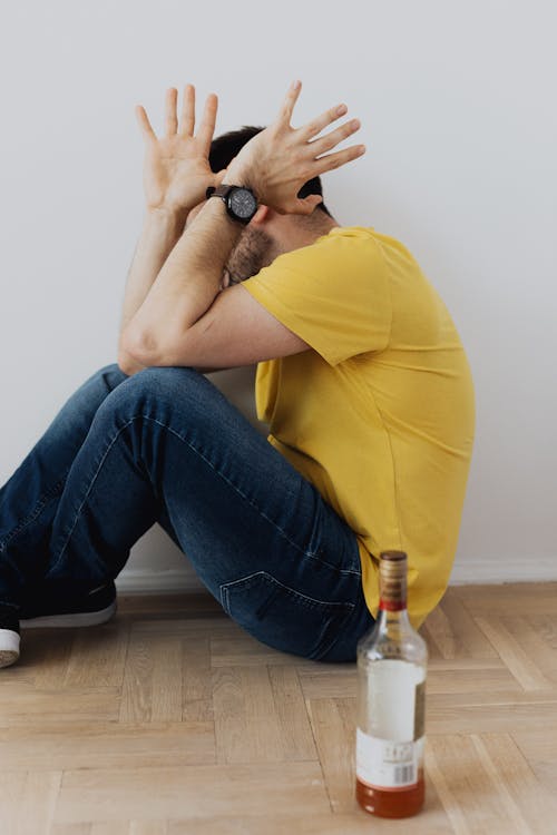 A Scared Man Sitting on the Floor next to a Whisky Bottle 