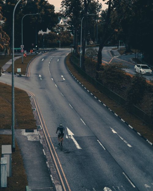 Free From above of distant unrecognizable person riding bicycle along empty asphalt road during sunrise Stock Photo