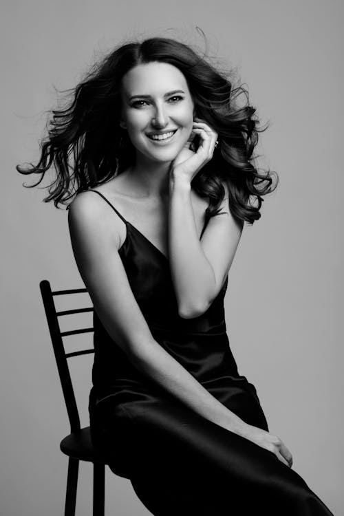 Grayscale Photo of a Smiling Woman Sitting on Chair