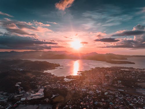 Drone view of bright sunlight illuminating mountains and calm lake with small town during sunset