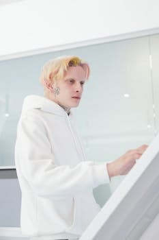 A stylish man in a white hoodie using a modern touchscreen in a bright indoor setting.