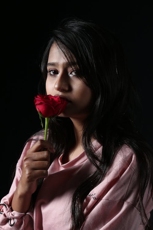 Calm serious woman with red flower looking at camera while thinking about problem