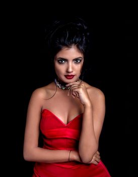 Portrait of a South Asian woman posing elegantly in a red dress against a black background.