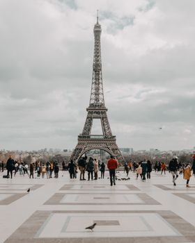 Wide shot of the Eiffel Tower surrounded by tourists on a cloudy day in Paris.