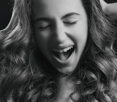Close-up of a woman with wavy hair exhibiting joy in black and white.