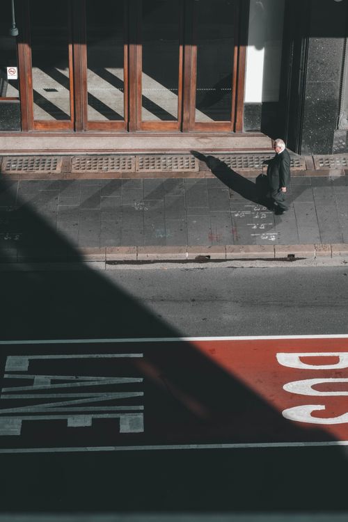 Free A senior man walks on a sunny sidewalk casting a long shadow, an urban scene captured from above in Sydney, Australia. Stock Photo