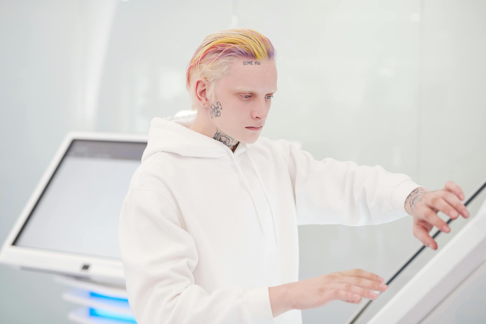 Portrait of a tattooed man with colored hair using a touchscreen kiosk in a modern setting.