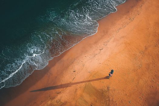 Drone view of person standing on wet sandy beach near foaming waves of ocean