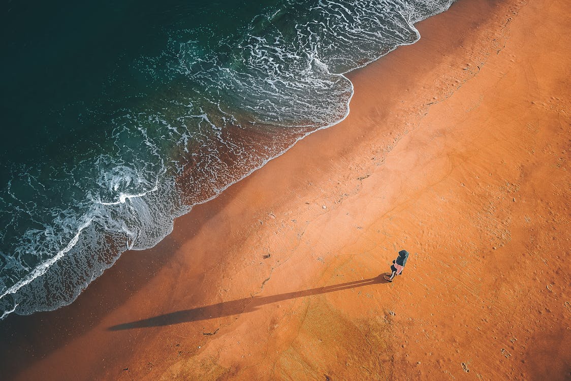 Free Drone view of person standing on wet sandy beach near foaming waves of ocean Stock Photo