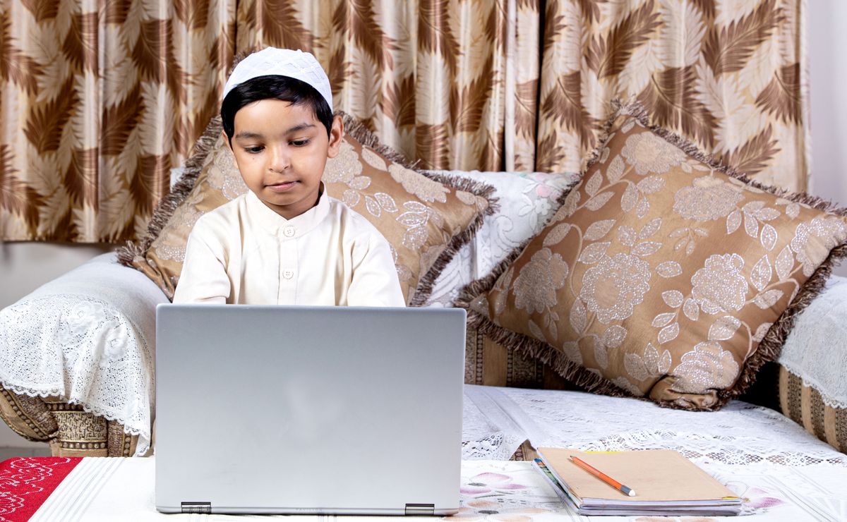 A young student in a live online Quran class, watching his tutor on a laptop