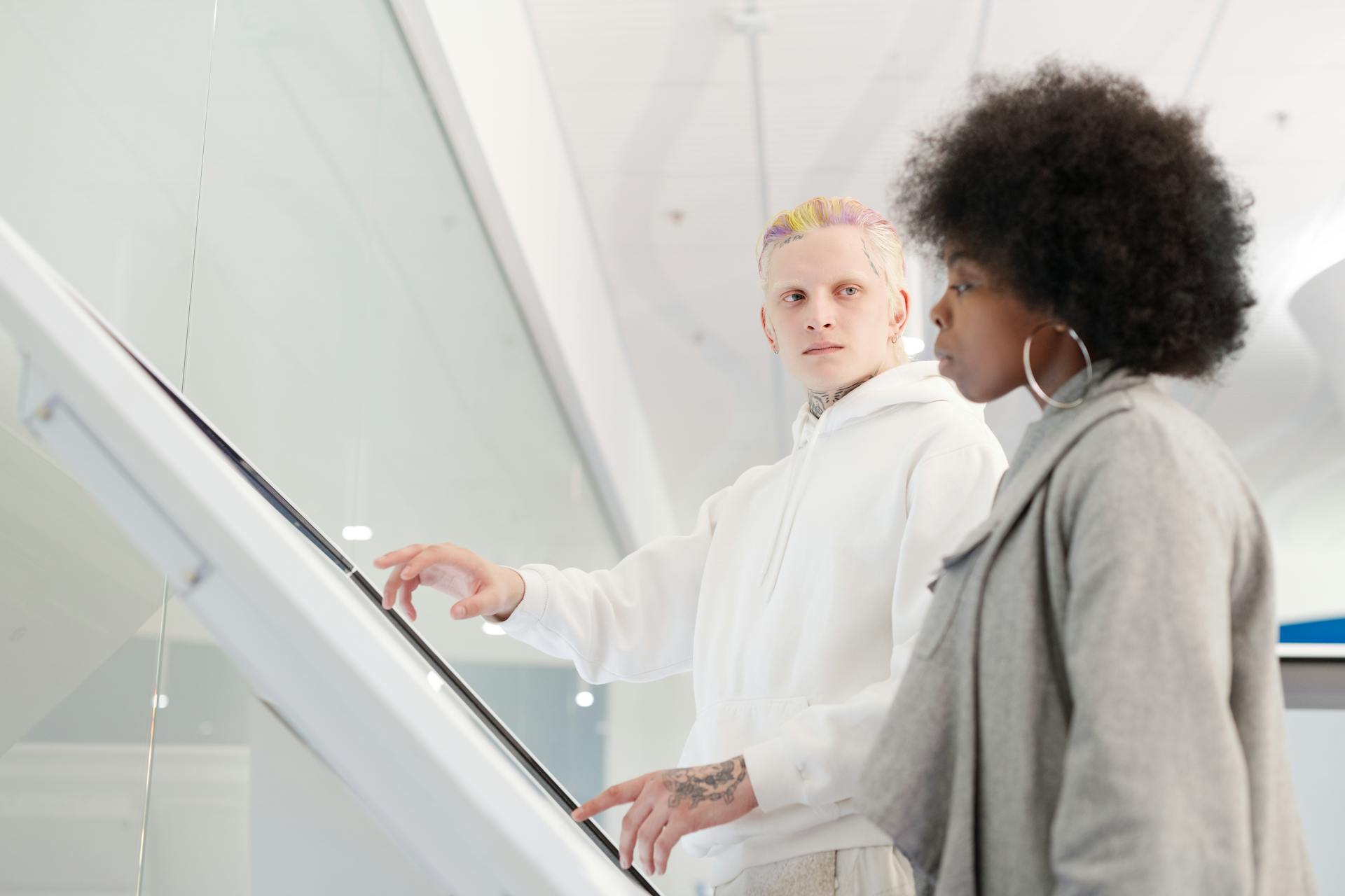 Two adults interact with a digital kiosk in a bright, contemporary indoor setting.