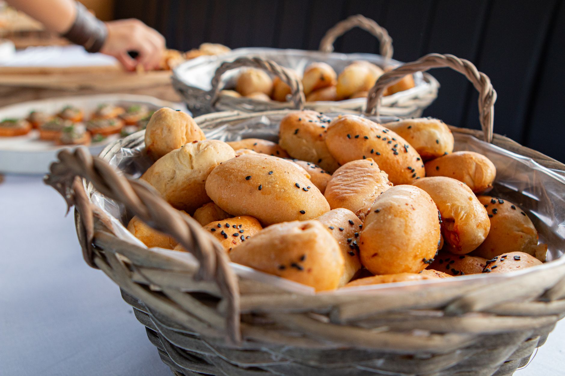 Close-up of freshly baked bread rolls with poppy seeds in woven wicker baskets, perfect for a bakery setting.
