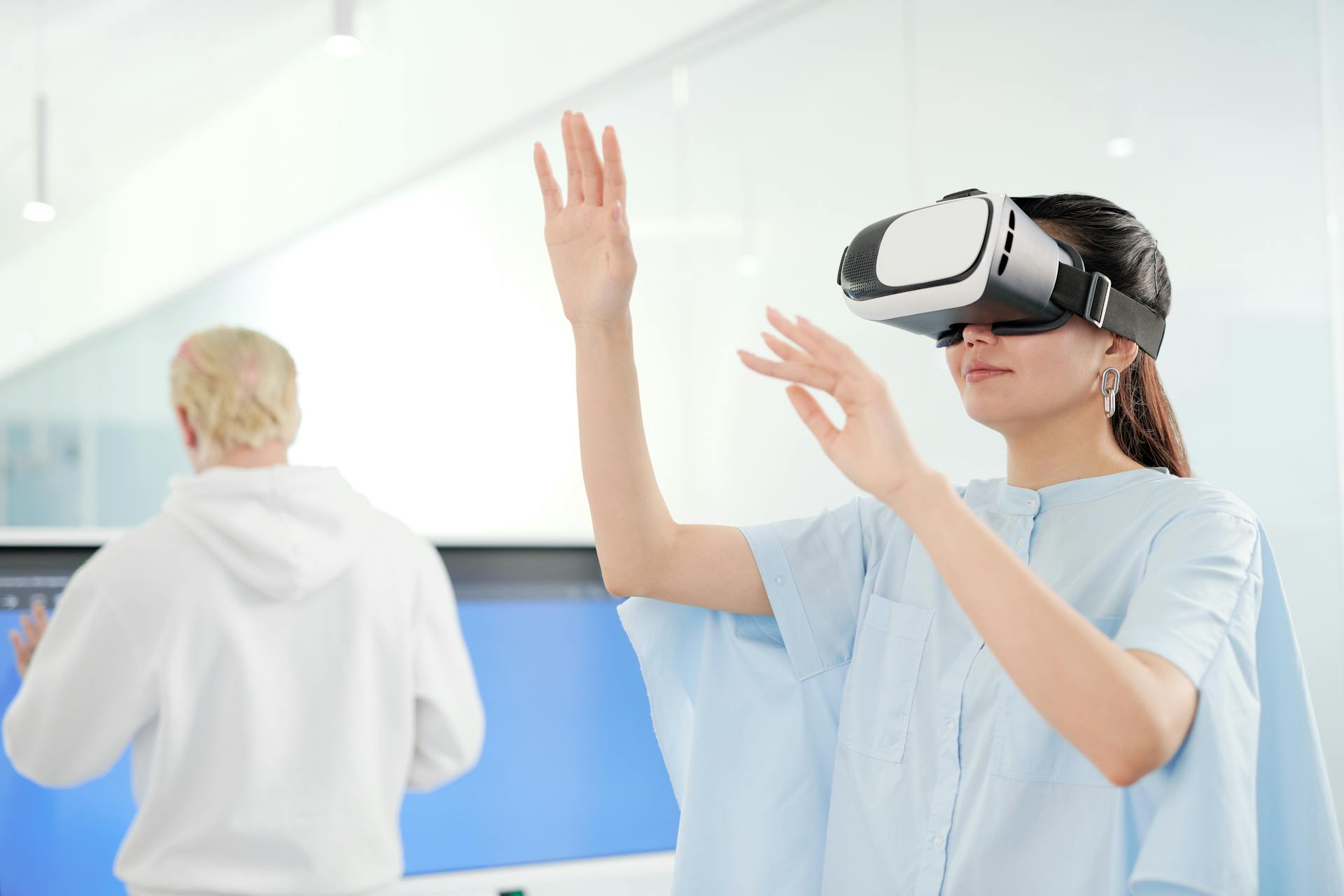 Asian woman in blue top exploring virtual reality technology indoors, gesturing and smiling.