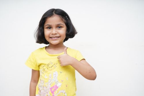 Free Cheerful young girl in a yellow shirt giving a thumbs up against a white background. Stock Photo